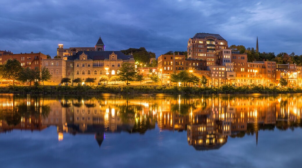 A cityscape at dusk with buildings reflecting on a calm river.
