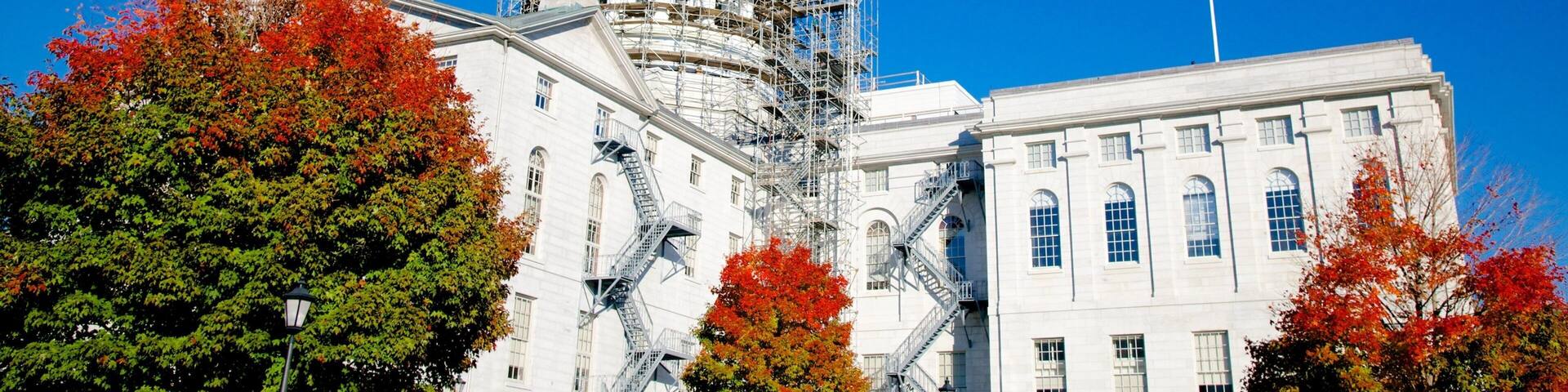 A historic building with a dome and scaffolding, surrounded by autumn trees.