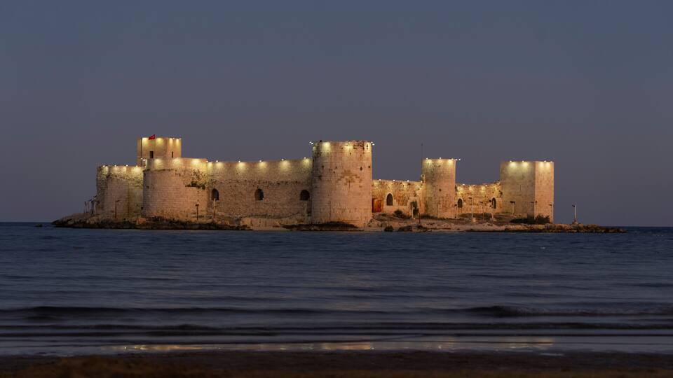 A fortified castle with multiple towers, situated on a small island surrounded by water.