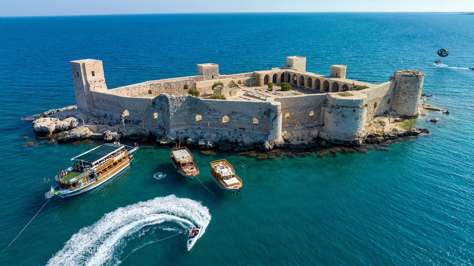A historic fort surrounded by clear blue waters with boats and a parasail.
