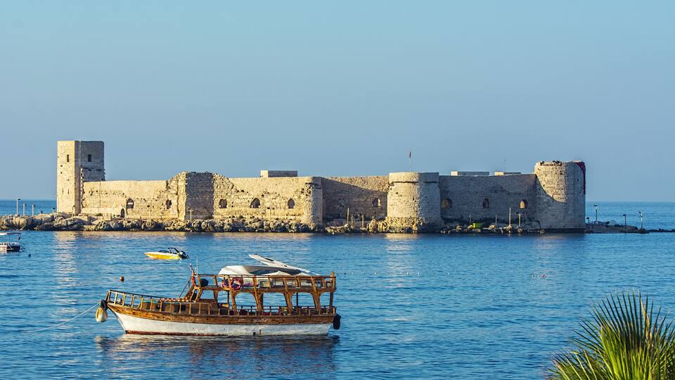 A historic stone fortress by the sea with a wooden boat anchored nearby.