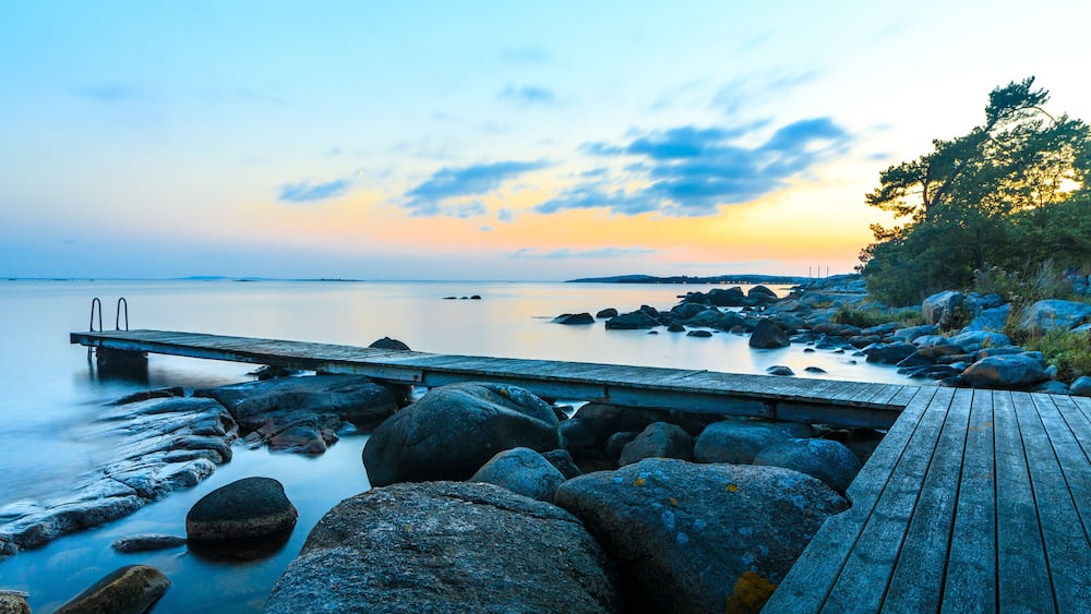 A wooden pier extending into calm waters with large rocks and a sunset in the background.