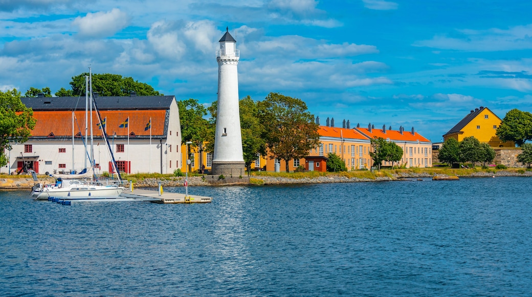 A lighthouse, a white building with a red roof, and a yellow building with a red roof by a body of water.