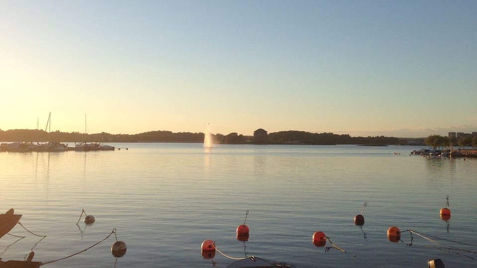 A calm harbor with boats docked and buoys floating on the water.