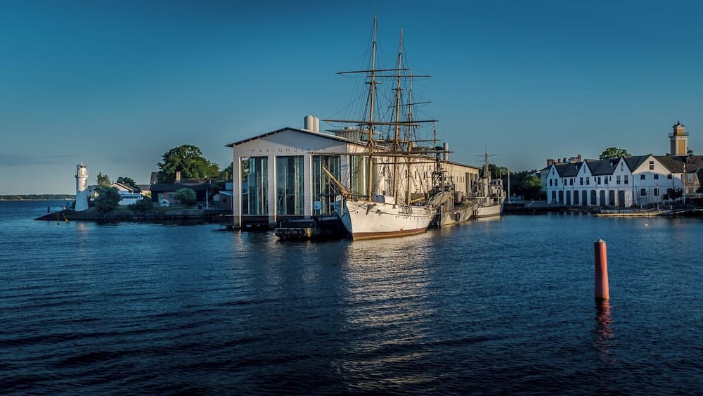 Un grand voilier était amarré dans un port, avec un phare et un musée en arrière-plan.