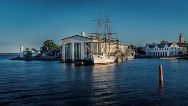 Un barco de gran altura atracado en un puerto con un faro y un museo al fondo.