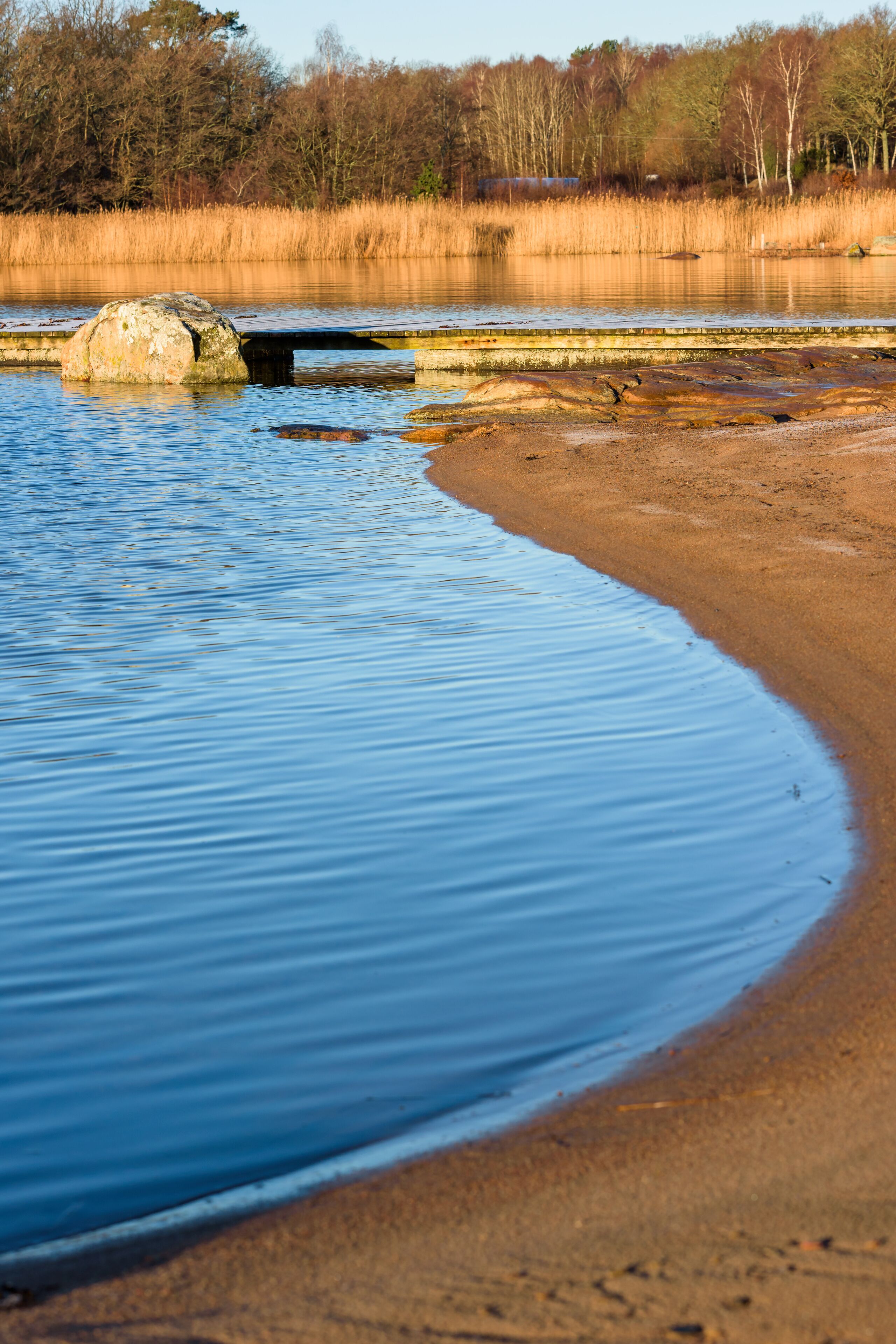 Sandy beach with wooden pier and granite boulder in the water. Location Nattraby, Karlskrona, Sweden.