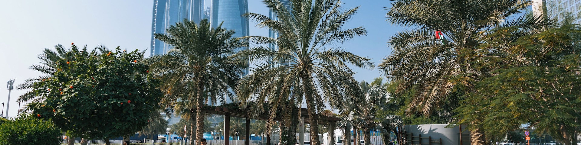 A cityscape with tall skyscrapers, palm trees, and a paved walkway.