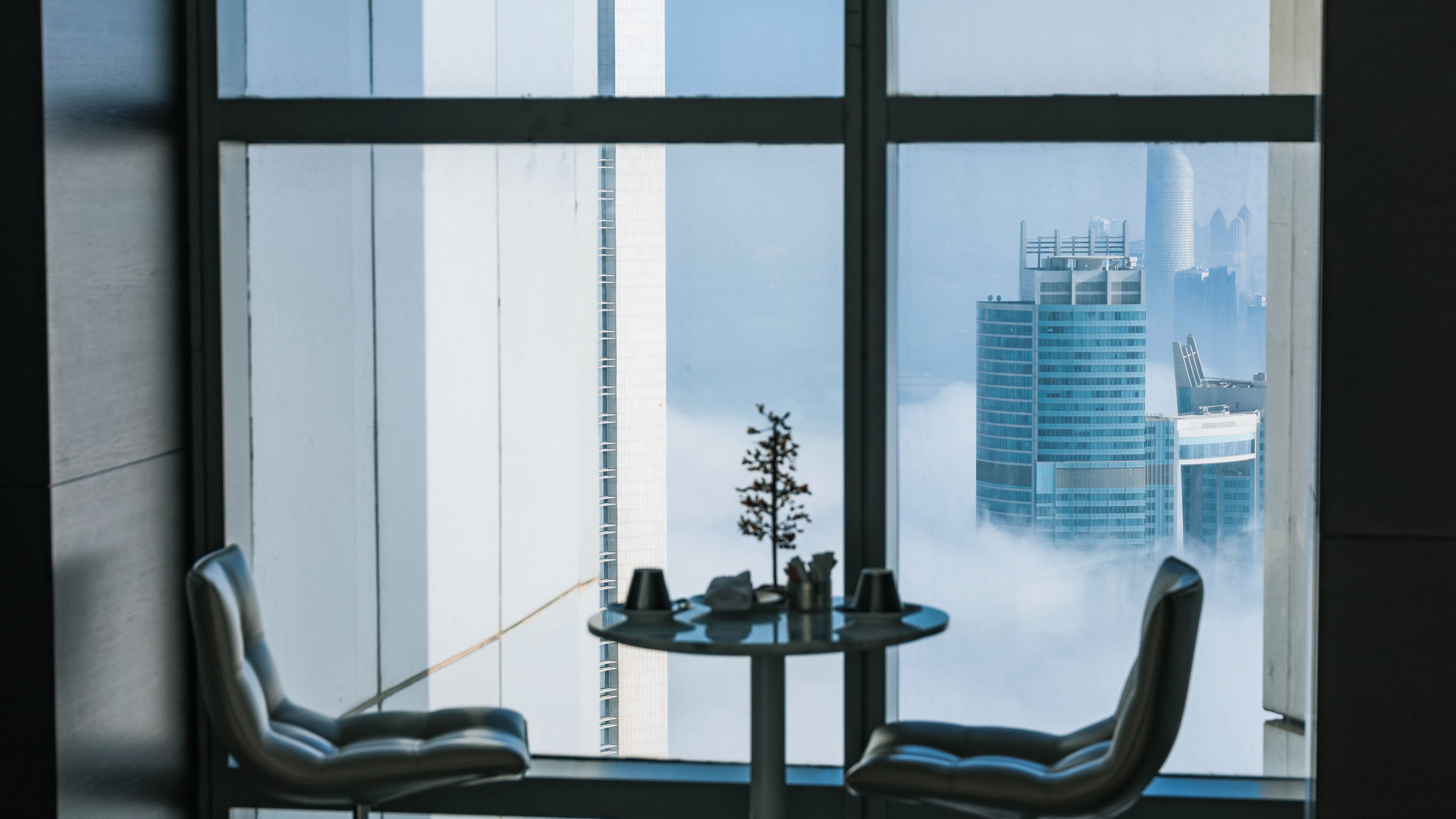 A view of a cityscape through a window with a table and chairs in the foreground.