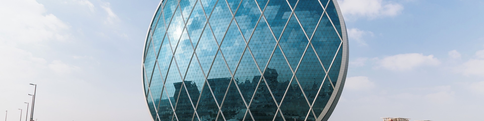 A modern spherical building with a glass facade, surrounded by palm trees and urban buildings.
