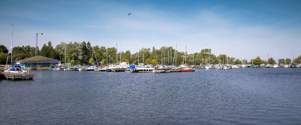 A marina with various boats docked, a clear blue sky, and a building in the background.
