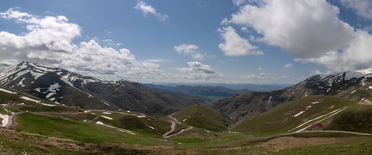 A mountainous landscape with snow-capped peaks, green valleys, and winding roads.