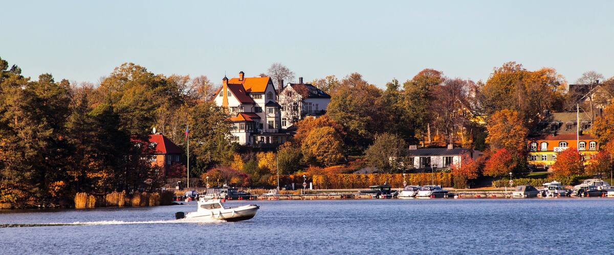 A lake with a boat, autumn-colored trees, and houses along the shore.