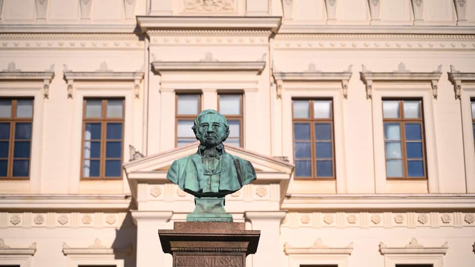 A bust sculpture on a pedestal with the inscription 'Sven Nilsson' in front of a classical building with ornate architectural details.