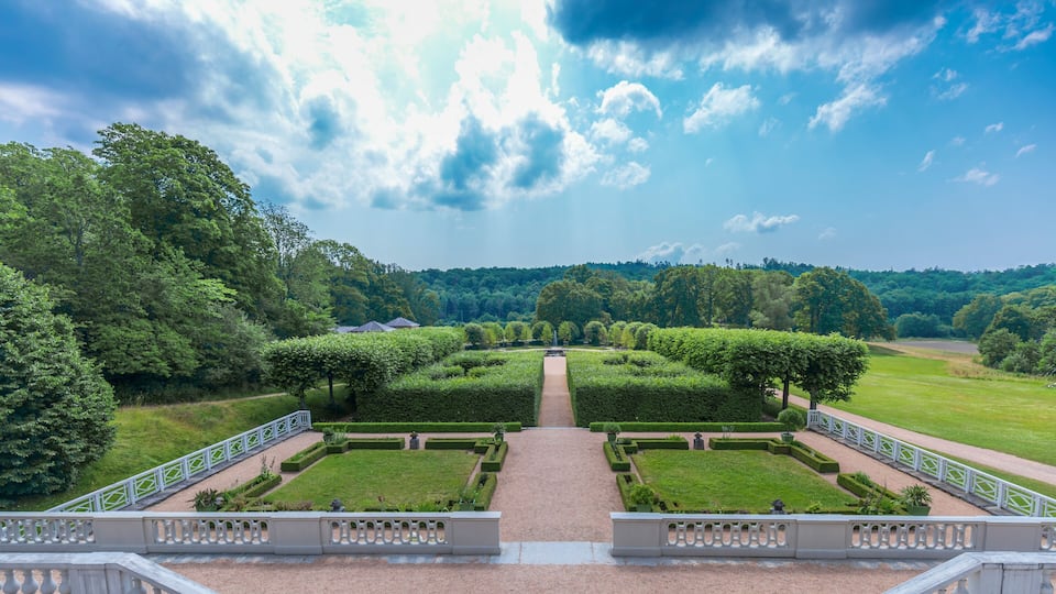 A formal garden with symmetrical hedges, a central pathway, and a staircase leading to a viewing platform.