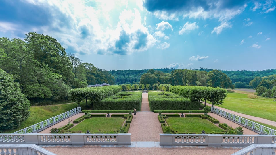 A formal garden with symmetrical hedges, a central pathway, and a staircase leading to a viewing platform.