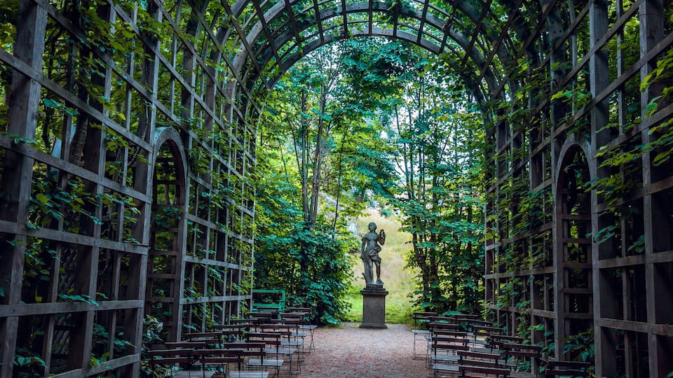 An arched wooden structure with benches and a statue in the center.