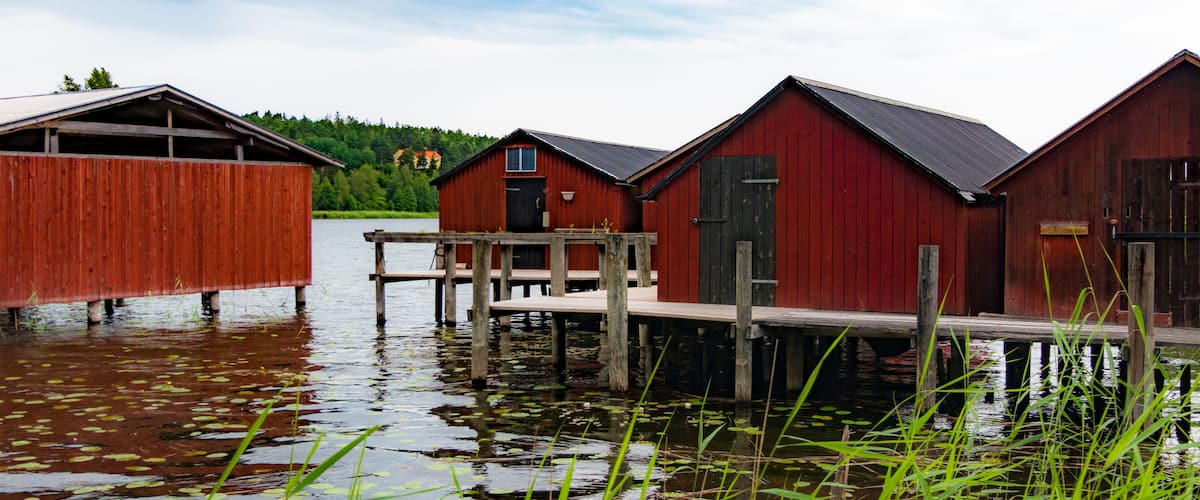 Wooden boathouses by a calm lake with surrounding greenery.