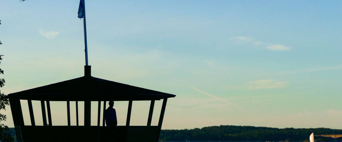 A gazebo on stilts by a lake with a sailboat in the distance.