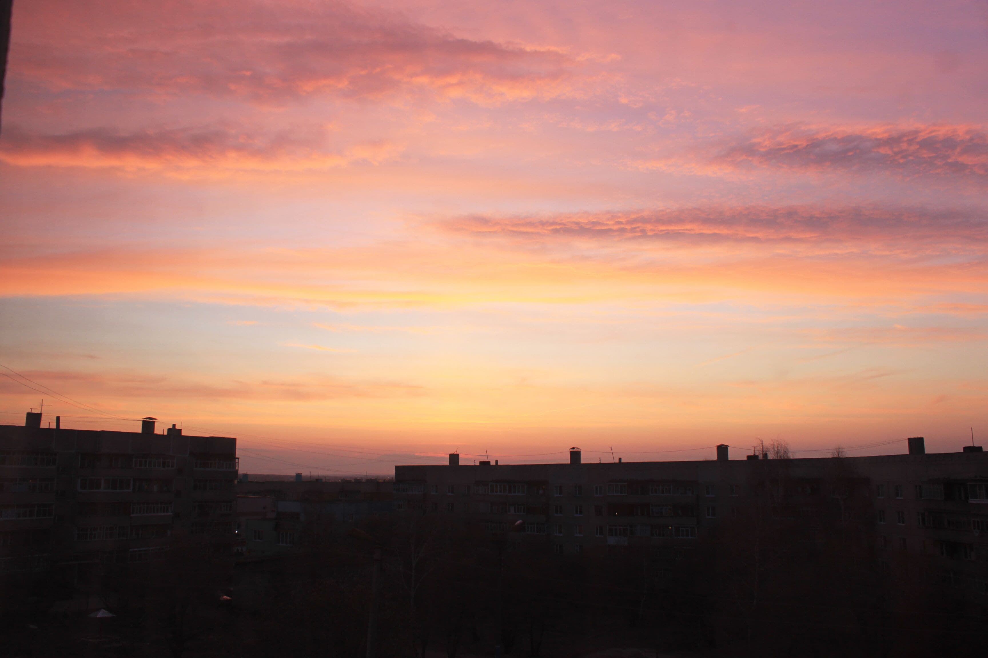 A sunset over a residential area with buildings silhouetted against a colorful sky.