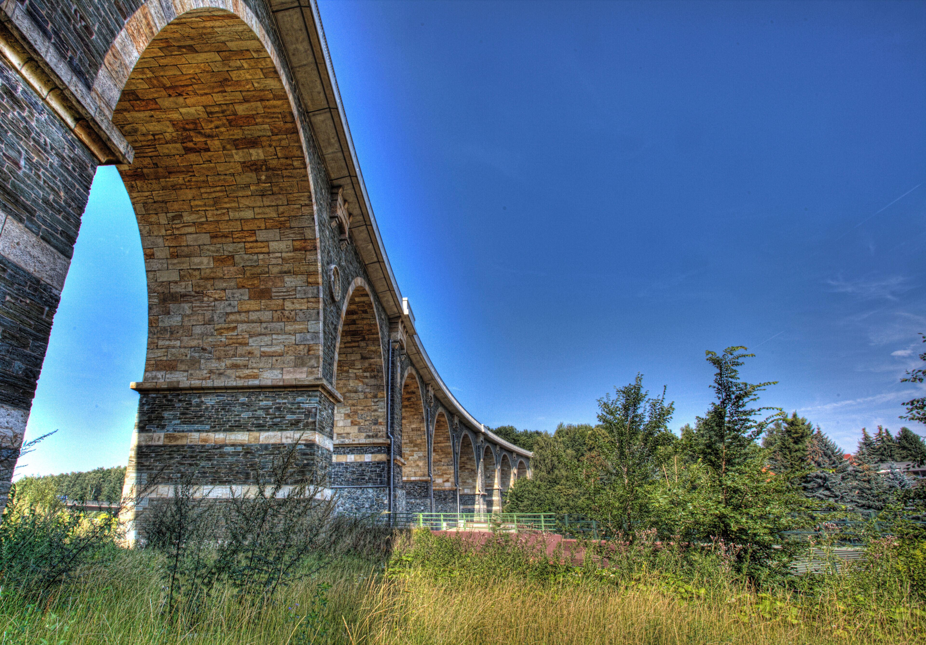 A stone viaduct with multiple arches, surrounded by greenery and trees.