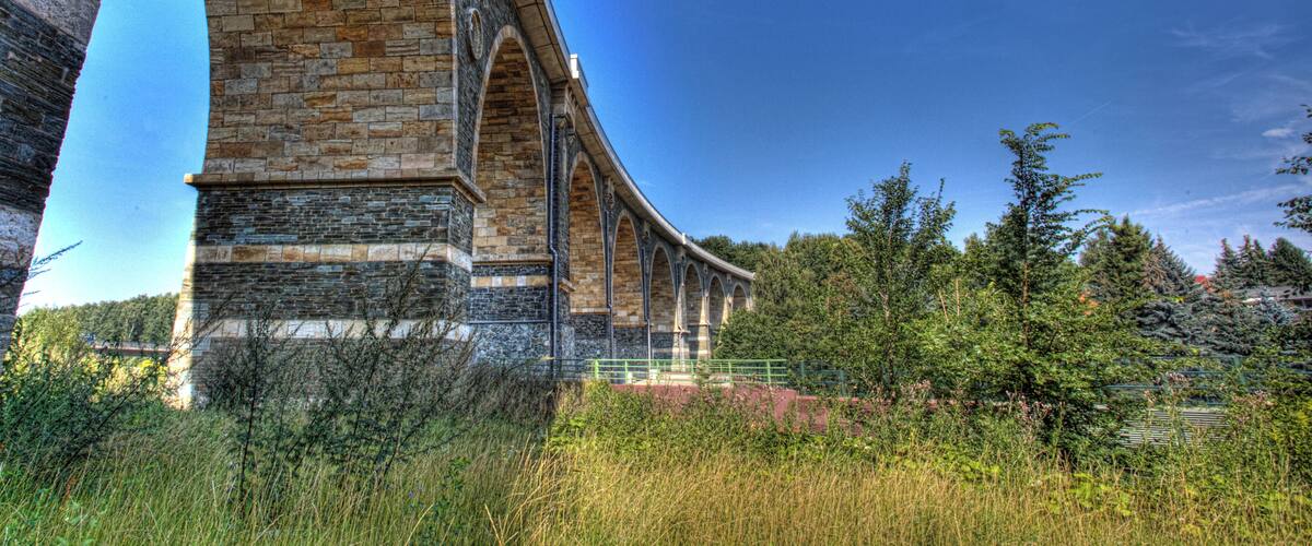 A stone viaduct with multiple arches, surrounded by greenery and trees.