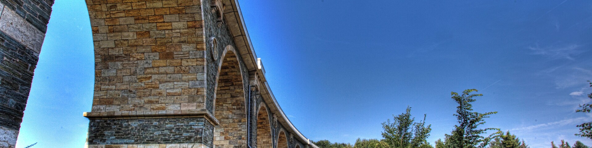A stone viaduct with multiple arches, surrounded by greenery and trees.