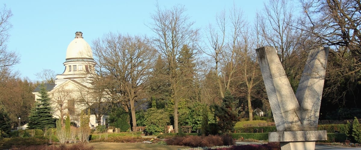 A park with a large building with a dome, a stone sculpture, and various landscaped gardens.