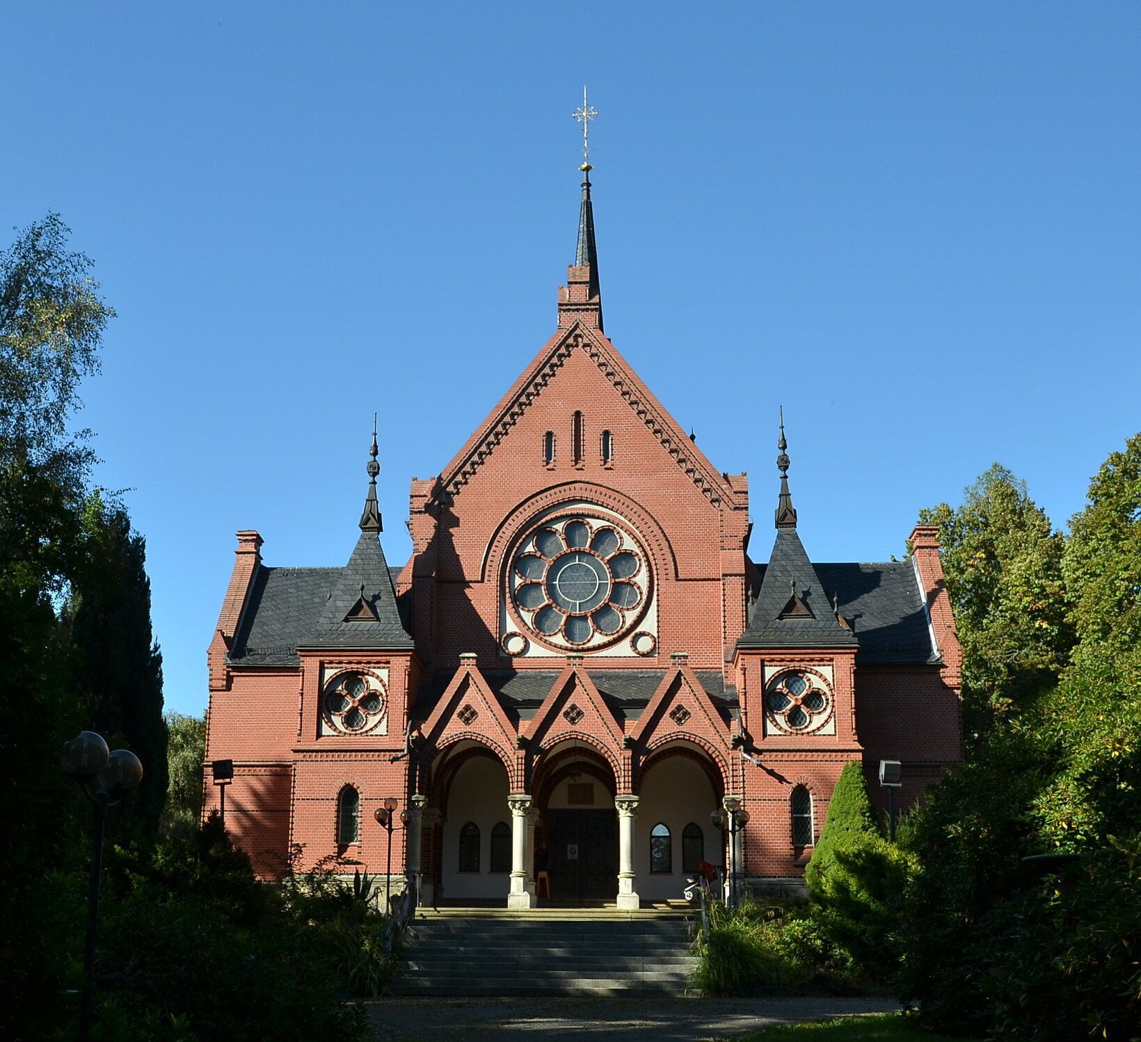 A large red brick church with a prominent circular window and two spires.