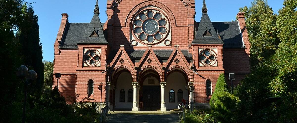 A large red brick church with a prominent circular window and two spires.