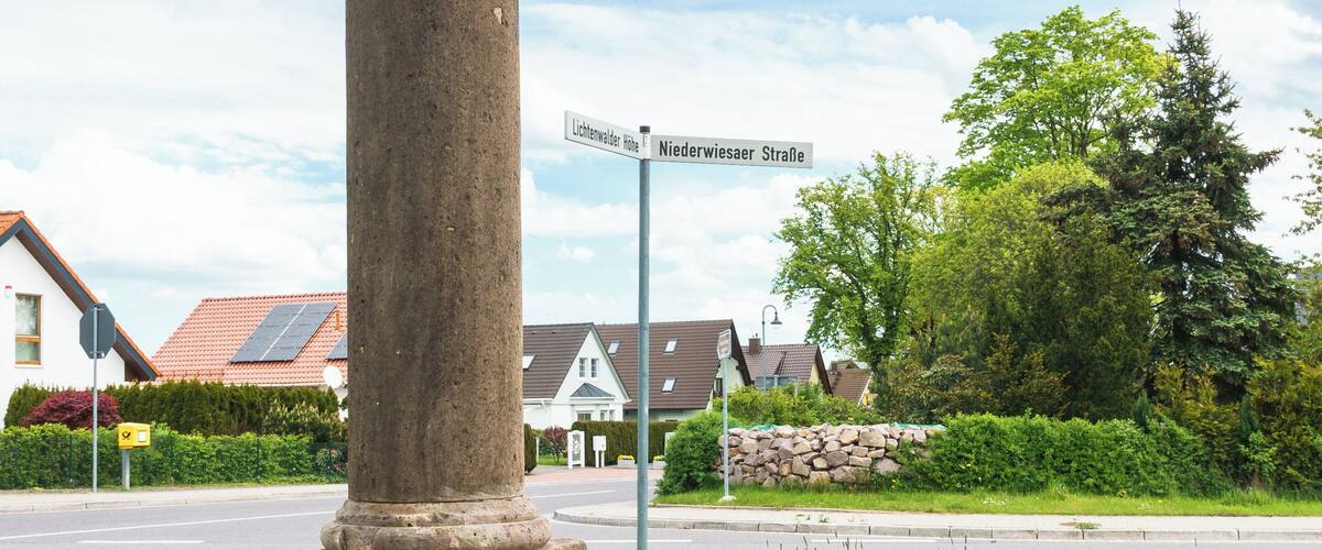 A stone monument with inscriptions, a street sign, and a bench in a grassy area with houses in the background.