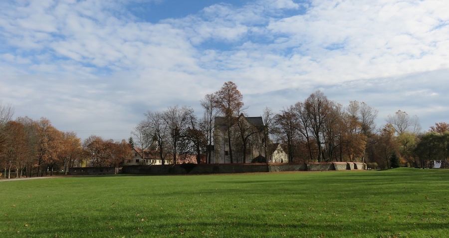 Un parque con un amplio campo verde, árboles y un edificio histórico al fondo.