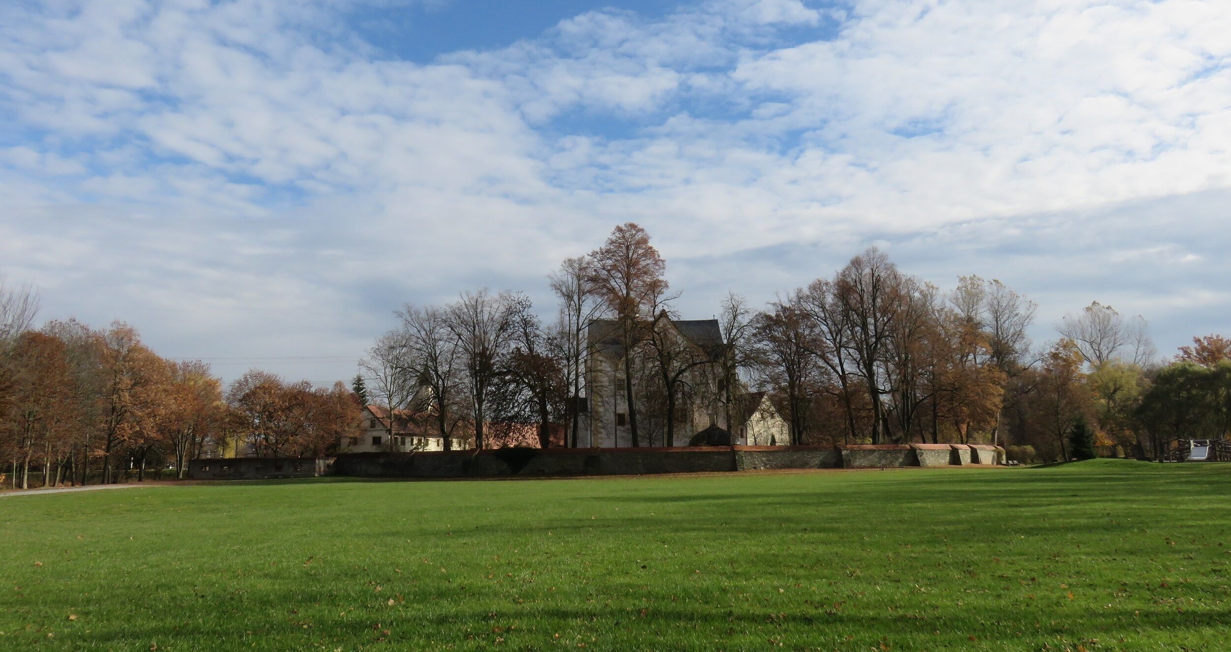 A park with a large green field, trees, and a historic building in the background.