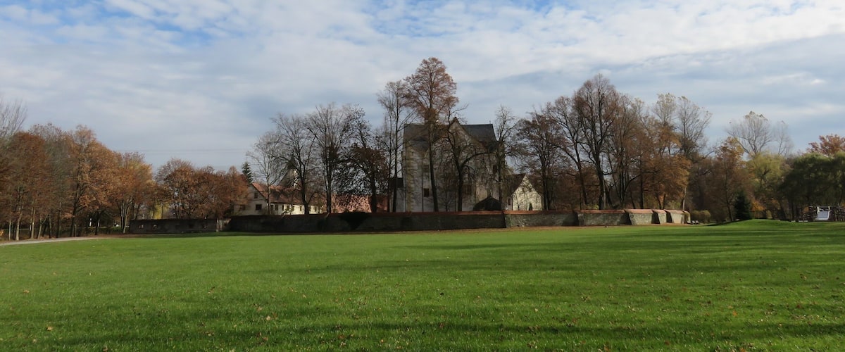 A park with a large green field, trees, and a historic building in the background.