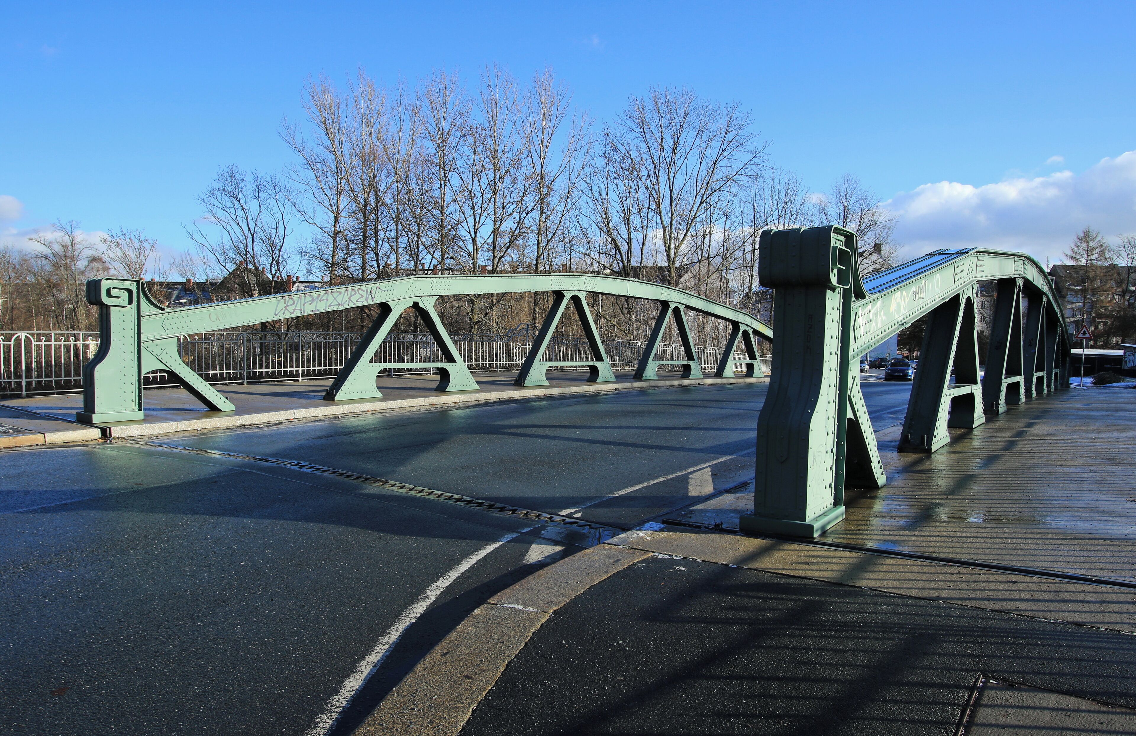 A green metal bridge with a pedestrian walkway.