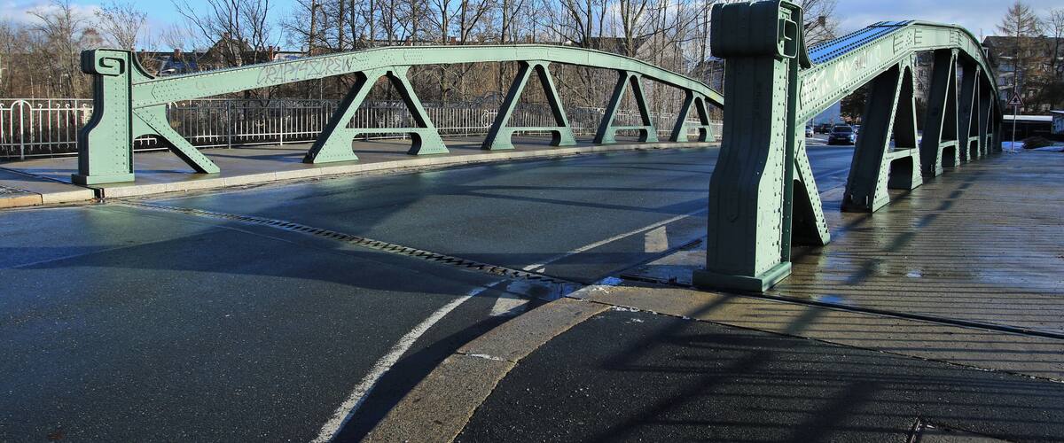 A green metal bridge with a pedestrian walkway.