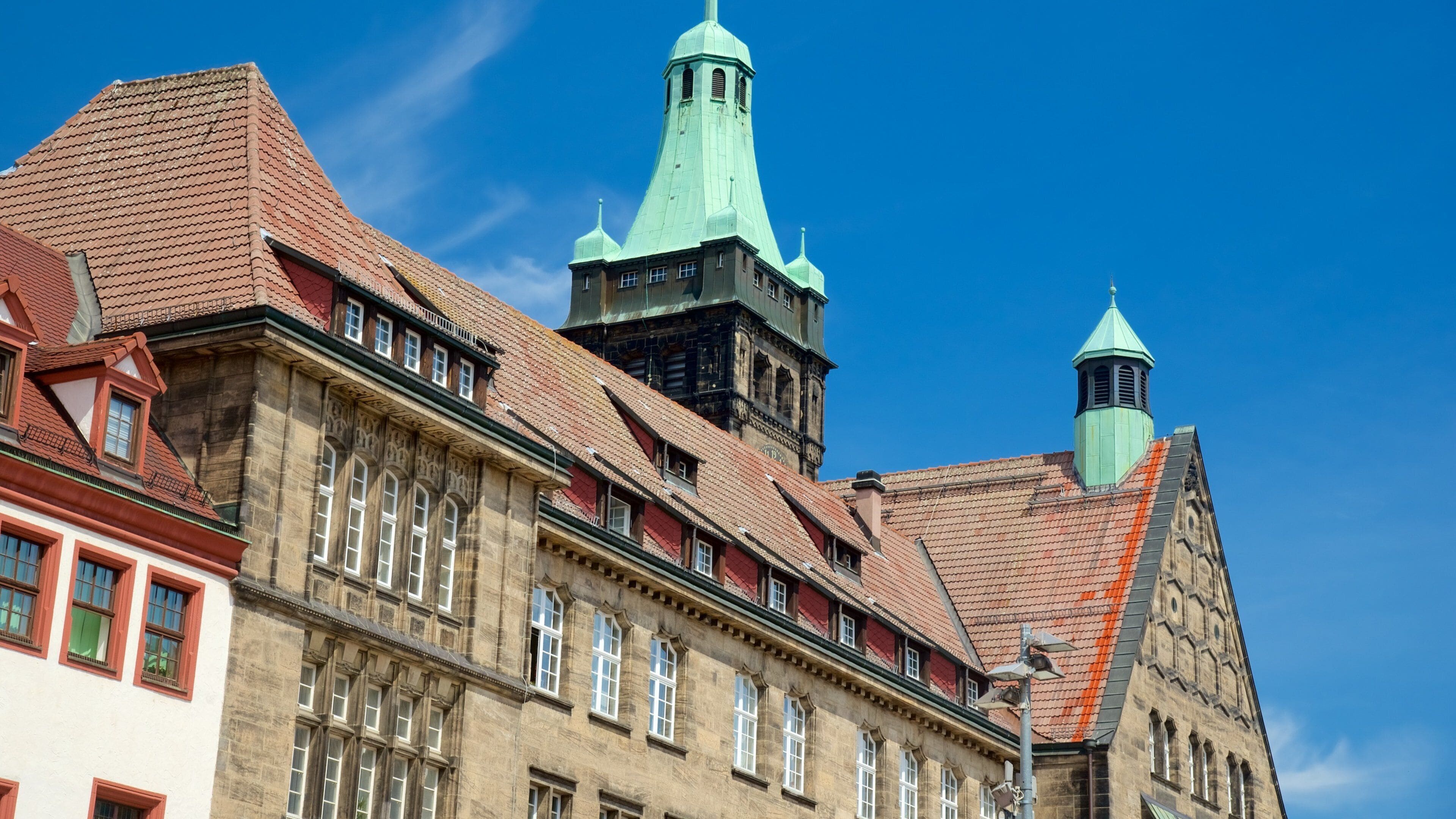 A historic building with a red-tiled roof and green spires.