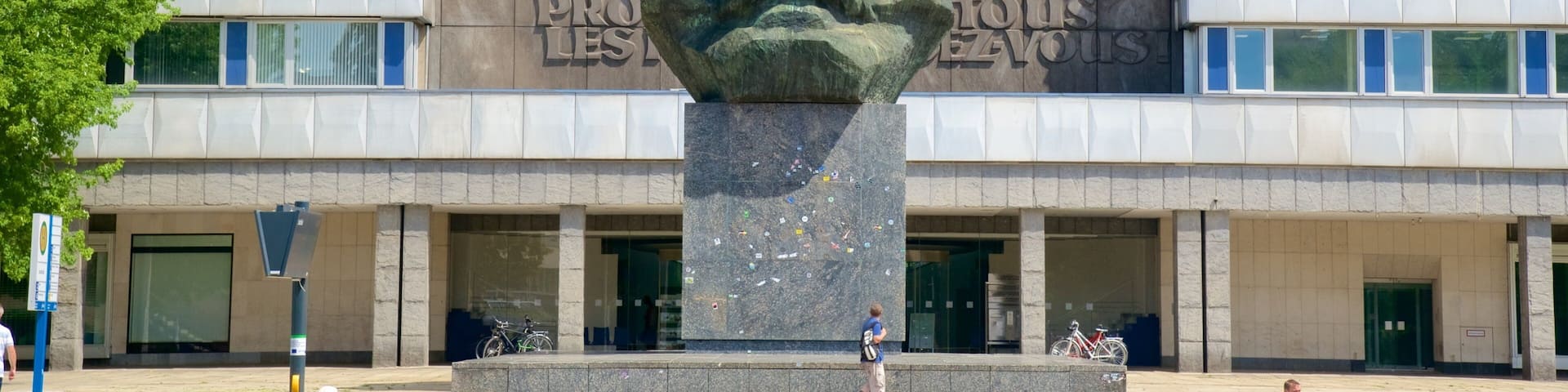 A large stone monument with inscriptions in multiple languages, set in front of a modern building with large windows.
