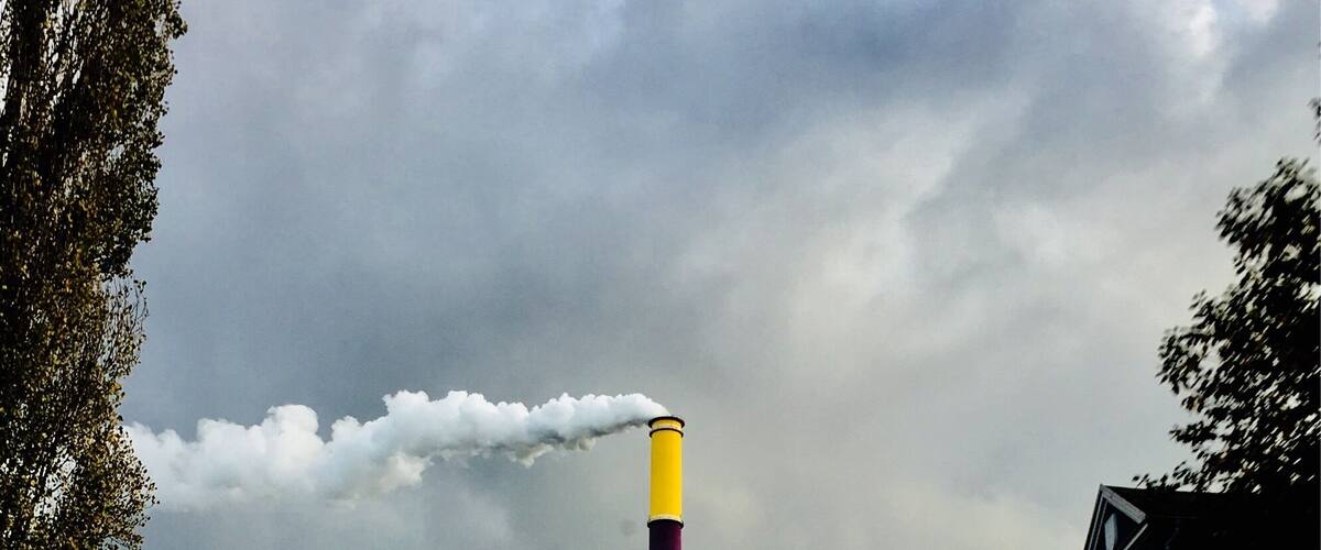 A tall, colorful chimney emitting smoke, surrounded by buildings and a cloudy sky.