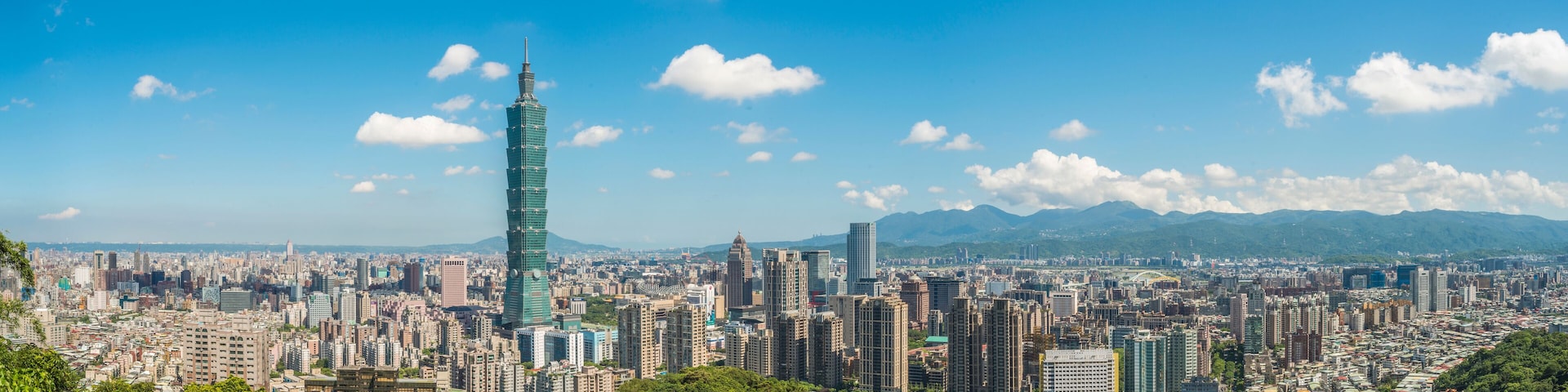 A cityscape with a prominent skyscraper, dense urban buildings, and mountains in the background.