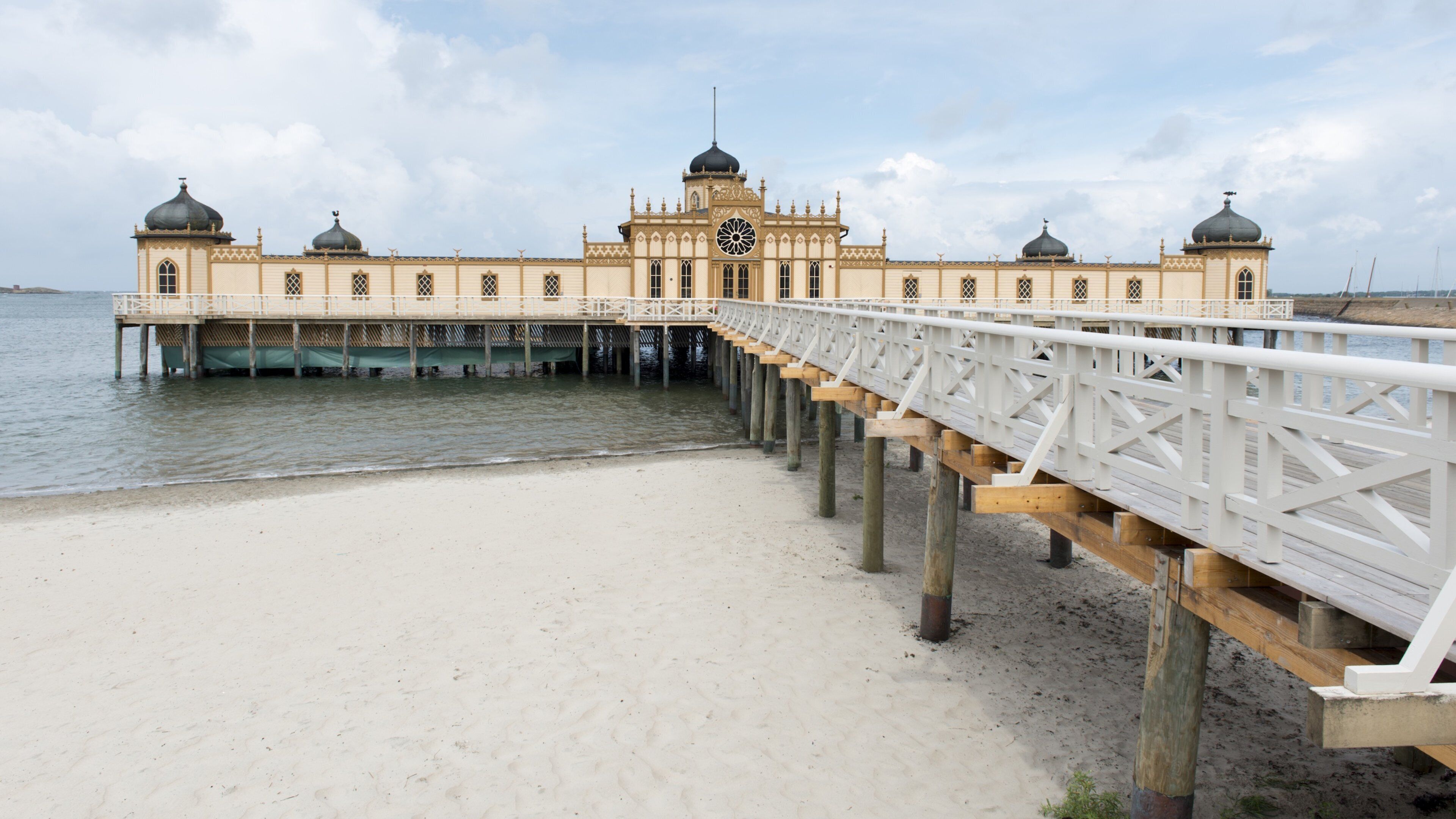 A pier leading to a large, ornate building with domes and a central clock tower.