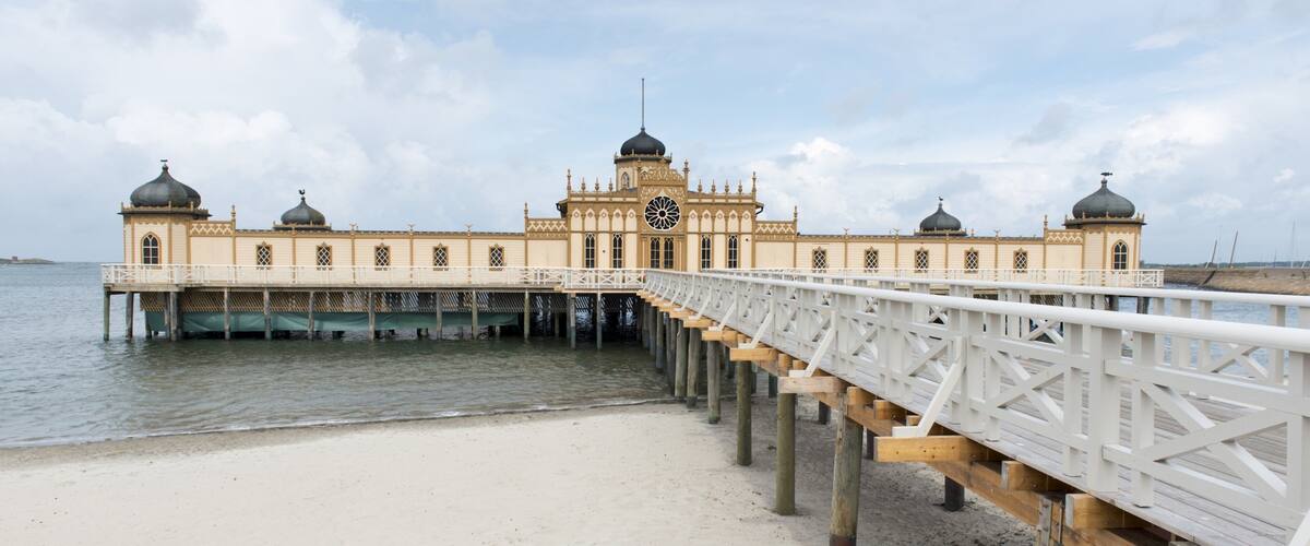 A pier leading to a large, ornate building with domes and a central clock tower.