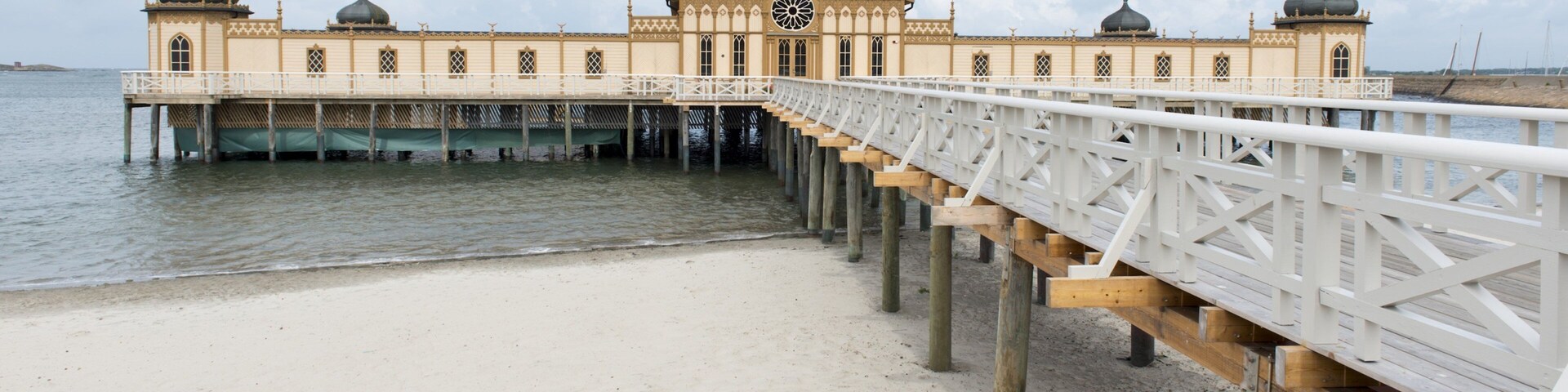 A pier leading to a large, ornate building with domes and a central clock tower.