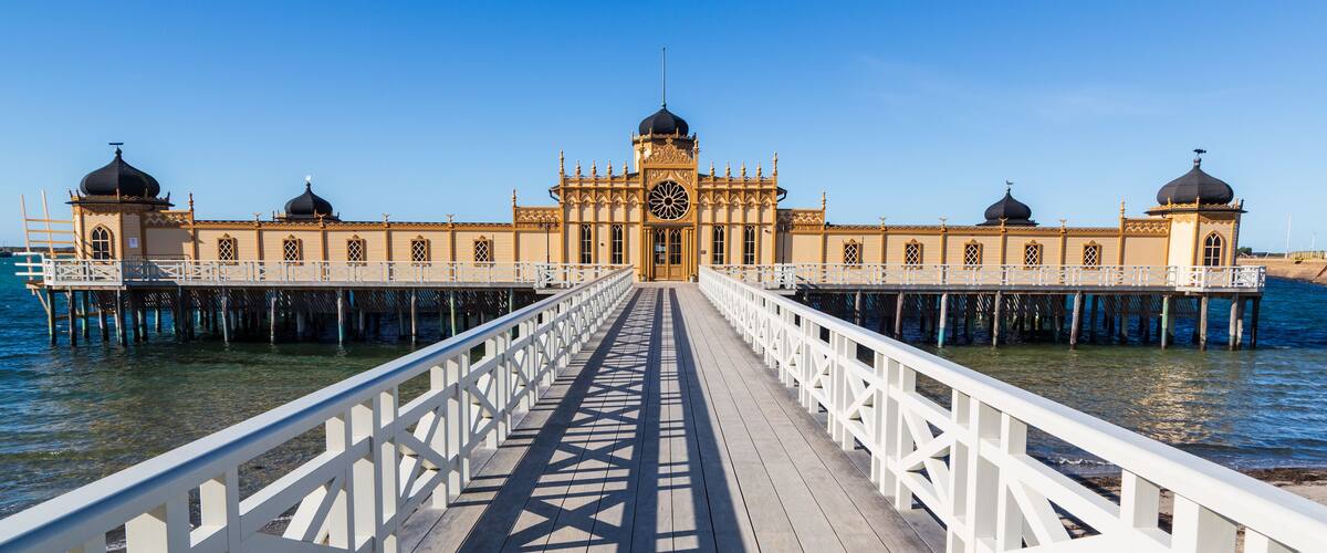 A wooden pier leading to a building with domed roofs and ornate architecture.