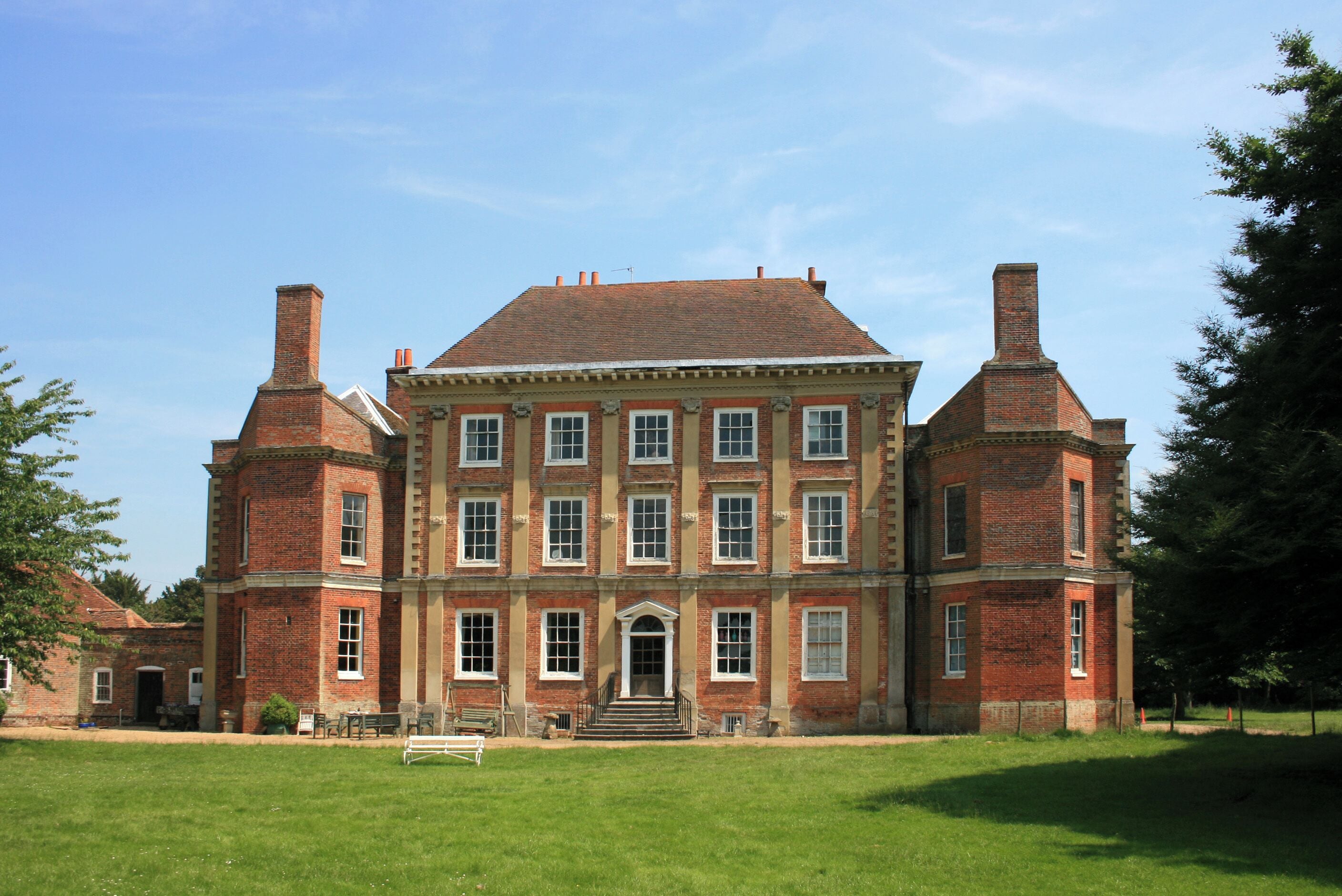 A large, historic brick building with a symmetrical facade, central entrance, and two prominent chimneys.