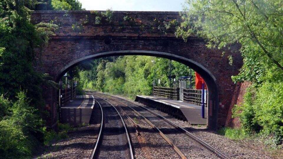 A railway track under a brick bridge surrounded by greenery.