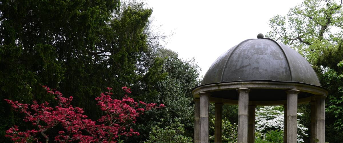 A gazebo with a dome roof, surrounded by lush greenery and flowering trees.