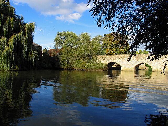A calm river with a stone bridge, trees, and a building in the background.