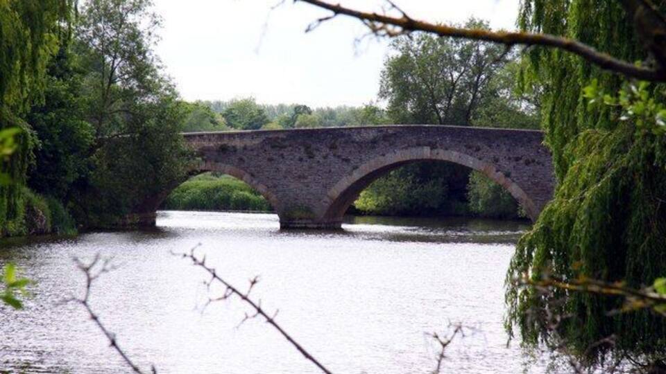 A stone bridge over a river, surrounded by trees and greenery.