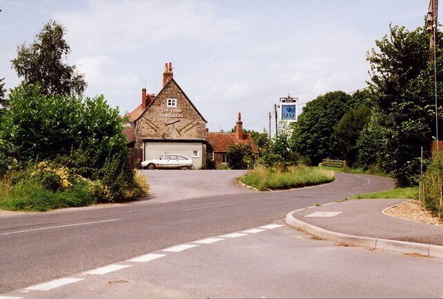 A rural road with a white car parked in front of a stone building with a garage.